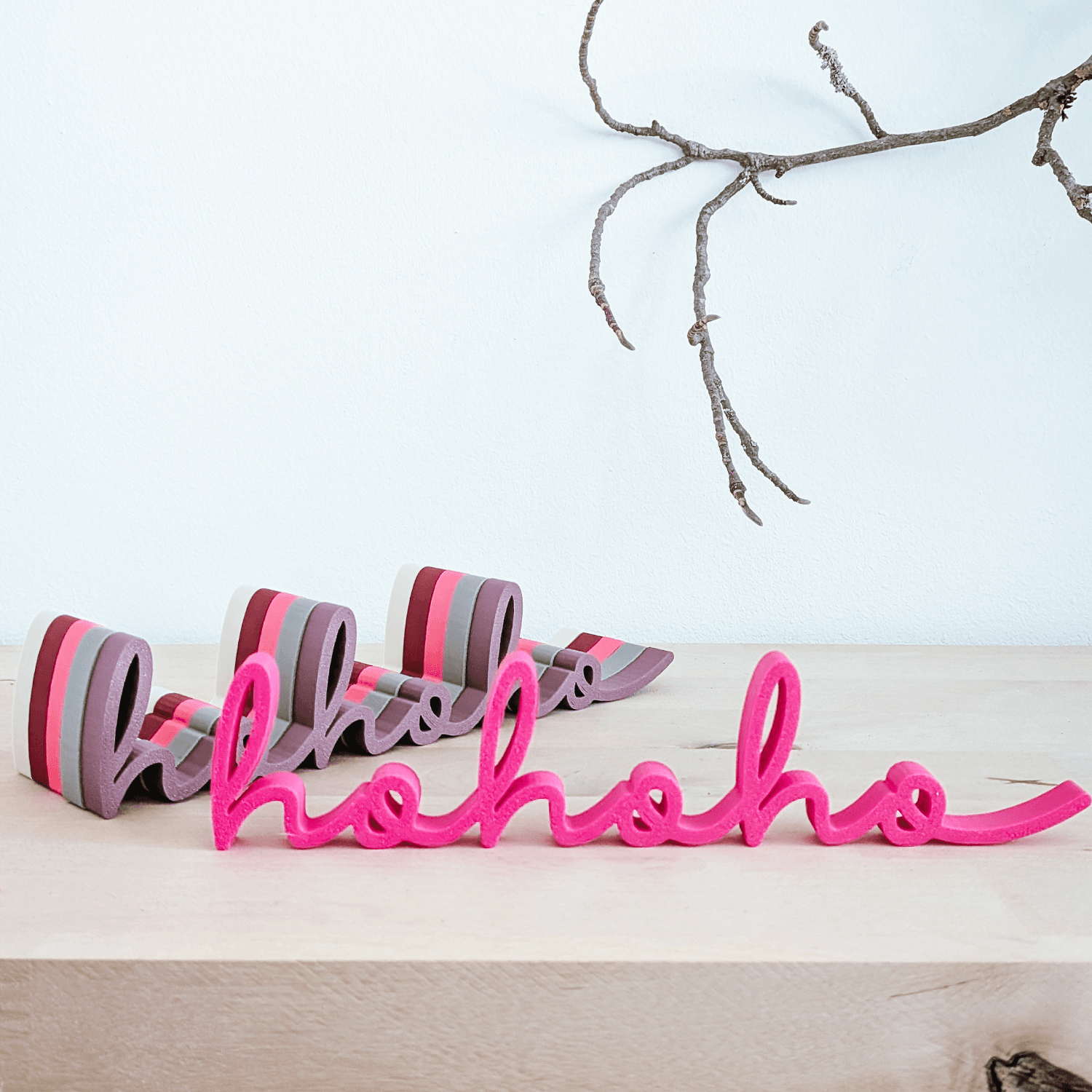 Mehrere 'hohoho' Schriftzüge in Pink sowie grau-mauve gestreiften Farben auf Holztisch