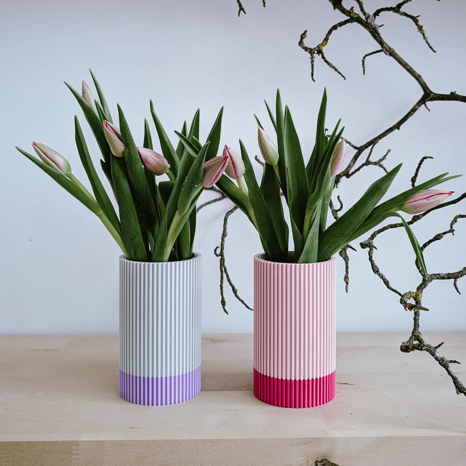 Vasen in Grau und Rosa mit Tulpen vor einem Zweig